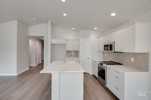 kitchen with vaulted ceiling, an island with sink, sink, white cabinets, and stainless steel appliances