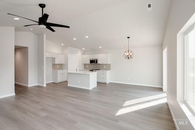 unfurnished living room featuring ceiling fan with notable chandelier, high vaulted ceiling, light hardwood / wood-style floors, and a wealth of natural light