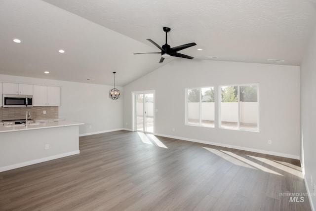 unfurnished living room featuring vaulted ceiling, ceiling fan with notable chandelier, sink, light hardwood / wood-style floors, and a textured ceiling