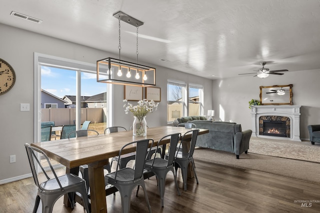 dining area featuring wood finished floors, visible vents, baseboards, a ceiling fan, and a glass covered fireplace