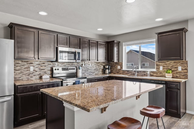 kitchen with light stone counters, a sink, a kitchen island, appliances with stainless steel finishes, and light wood-type flooring