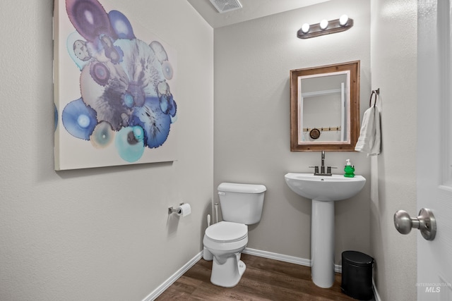 half bathroom featuring visible vents, toilet, a sink, wood finished floors, and baseboards