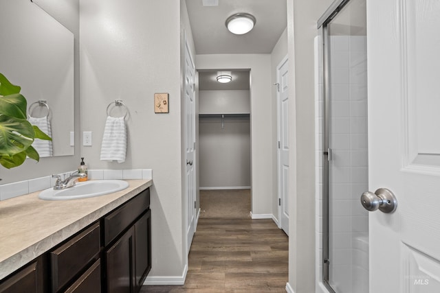 full bath with wood finished floors, vanity, baseboards, a spacious closet, and a stall shower