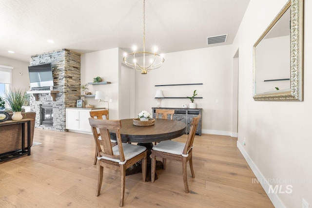 dining space featuring an inviting chandelier, light wood finished floors, a fireplace, baseboards, and visible vents