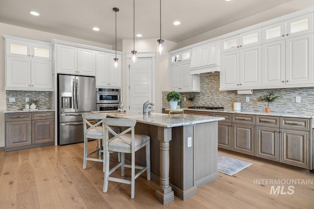 kitchen with white cabinets, light wood-type flooring, glass insert cabinets, tasteful backsplash, and appliances with stainless steel finishes