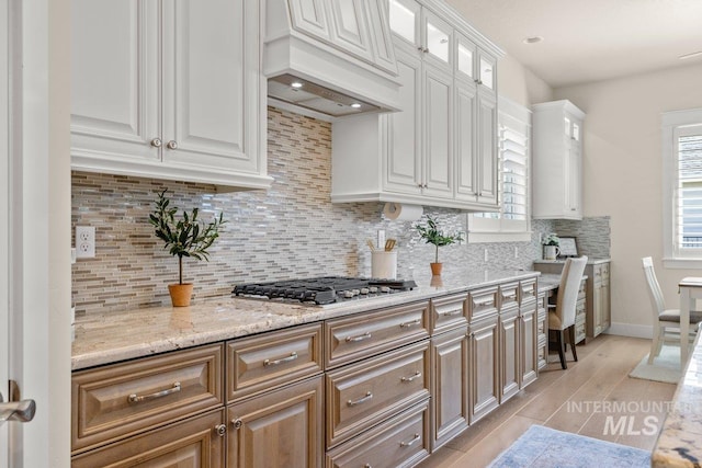 kitchen with white cabinets, light wood finished floors, premium range hood, decorative backsplash, and stainless steel gas cooktop