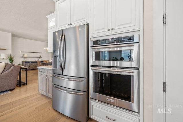 kitchen with open floor plan, glass insert cabinets, white cabinetry, light wood-style flooring, and appliances with stainless steel finishes