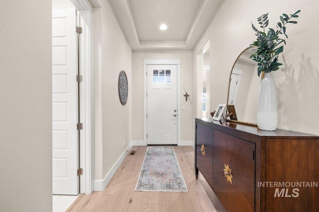 foyer entrance with a raised ceiling, light wood-style flooring, visible vents, and baseboards
