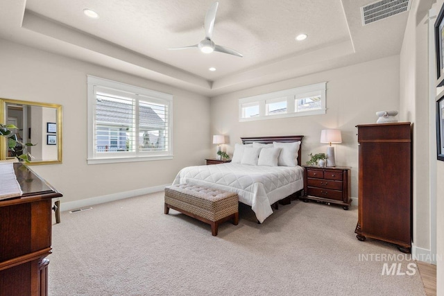 bedroom with light carpet, a tray ceiling, baseboards, visible vents, and recessed lighting