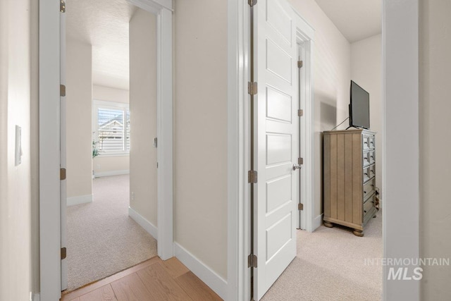 hall featuring light colored carpet, baseboards, and light wood-style flooring
