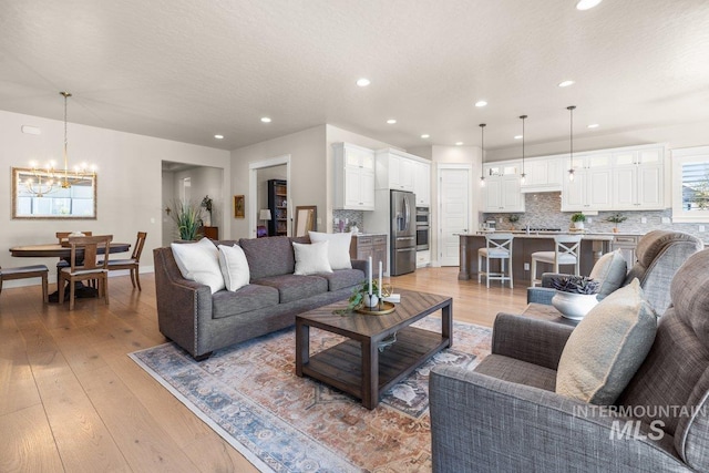 living area with light wood-style flooring, baseboards, recessed lighting, and a notable chandelier