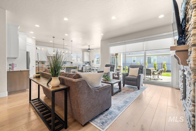 living room featuring recessed lighting, a stone fireplace, and light wood-style flooring