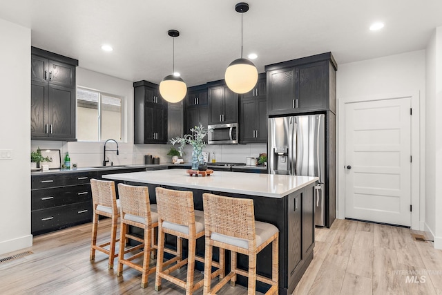 kitchen featuring sink, hanging light fixtures, appliances with stainless steel finishes, a kitchen island, and light wood-type flooring