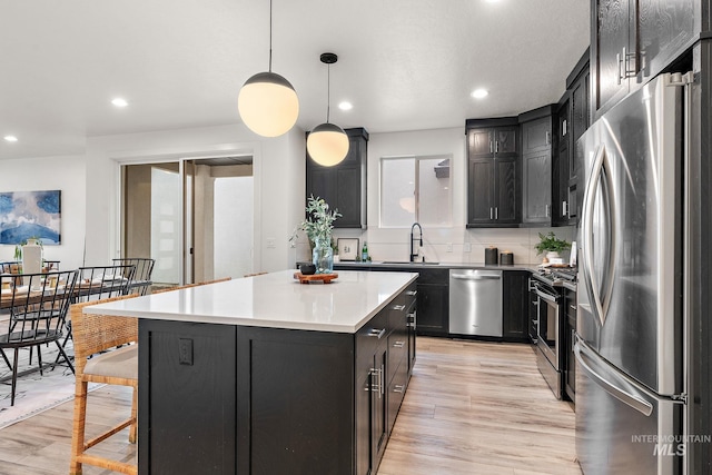 kitchen with light hardwood / wood-style floors, a center island, hanging light fixtures, and appliances with stainless steel finishes