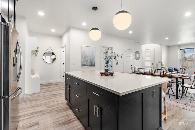 kitchen featuring a kitchen bar, a center island, hanging light fixtures, and stainless steel refrigerator with ice dispenser