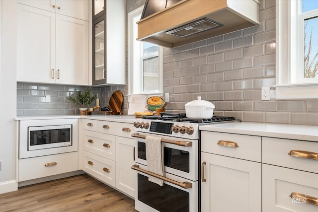 kitchen with double oven range, white cabinets, light countertops, built in microwave, and custom exhaust hood