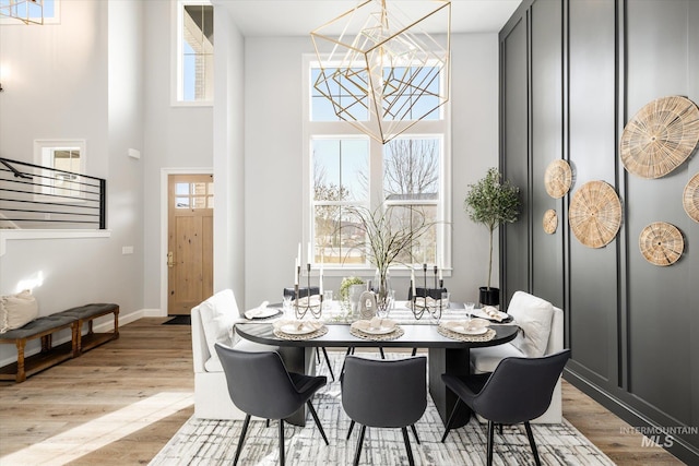 dining area featuring a high ceiling, light wood-style floors, baseboards, and a chandelier