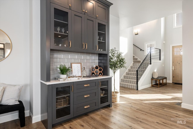 bar featuring stairway, backsplash, baseboards, and light wood-style floors