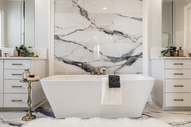 bathroom featuring stone wall, a freestanding tub, marble finish floor, and vanity