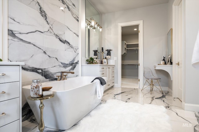 bathroom with vanity, stone wall, a freestanding tub, a walk in closet, and marble finish floor