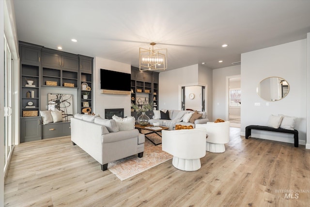 living room with a glass covered fireplace, an inviting chandelier, recessed lighting, and wood finished floors