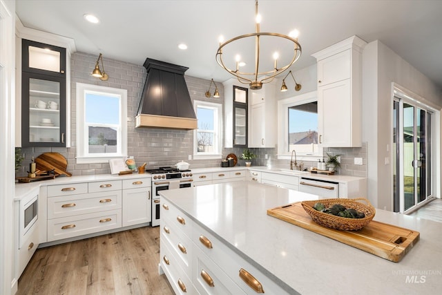 kitchen with custom range hood, backsplash, white appliances, white cabinets, and glass insert cabinets