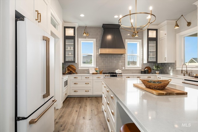 kitchen featuring light wood-style flooring, custom range hood, backsplash, white cabinetry, and high end white refrigerator