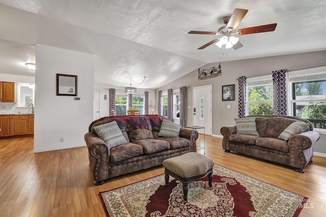 living room featuring light wood-type flooring, baseboards, vaulted ceiling, and a ceiling fan