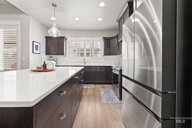 kitchen with light countertops, stainless steel appliances, dark brown cabinets, and light wood finished floors