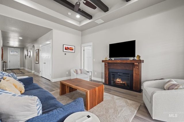 living area with beamed ceiling, baseboards, ceiling fan, wood finished floors, and a glass covered fireplace