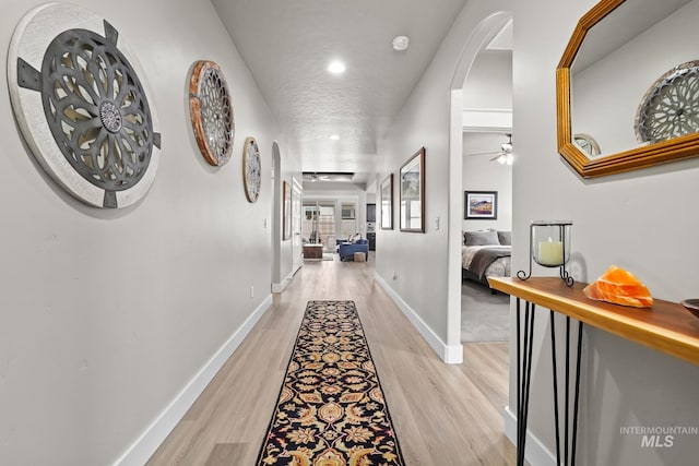 corridor featuring light wood-style flooring, arched walkways, baseboards, and recessed lighting