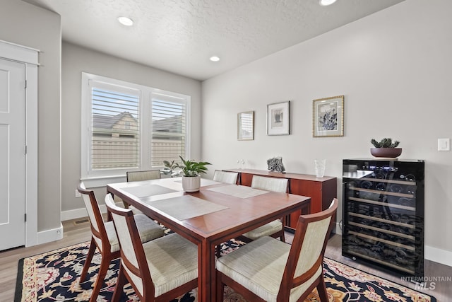 dining space with wine cooler, a textured ceiling, baseboards, light wood-style floors, and recessed lighting