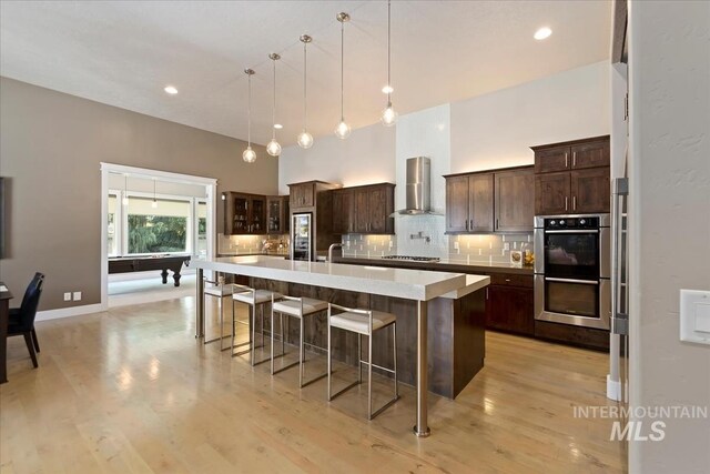 4307 W Briar Rock Ct, Eagle, ID 83616 - kitchen featuring wall chimney exhaust hood, appliances with stainless steel finishes, decorative backsplash, light countertops, and a kitchen breakfast bar