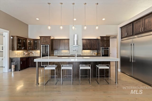 4307 W Briar Rock Ct, Eagle, ID 83616 - kitchen with appliances with stainless steel finishes, wall chimney range hood, dark brown cabinetry, decorative backsplash, and light countertops