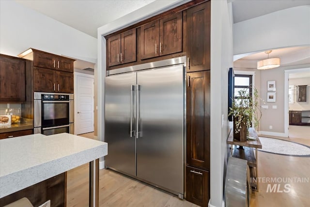 4307 W Briar Rock Ct, Eagle, ID 83616 - kitchen featuring stainless steel appliances, arched walkways, dark brown cabinets, light wood-type flooring, and light stone counters