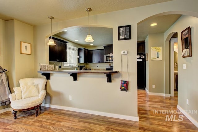 kitchen featuring a kitchen bar, stainless steel microwave, a textured ceiling, light wood-style floors, and baseboards