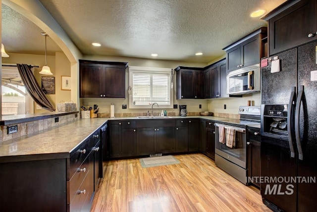 kitchen featuring light wood finished floors, a peninsula, a sink, black appliances, and dark brown cabinets