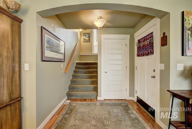 foyer with arched walkways, stairs, baseboards, and wood finished floors