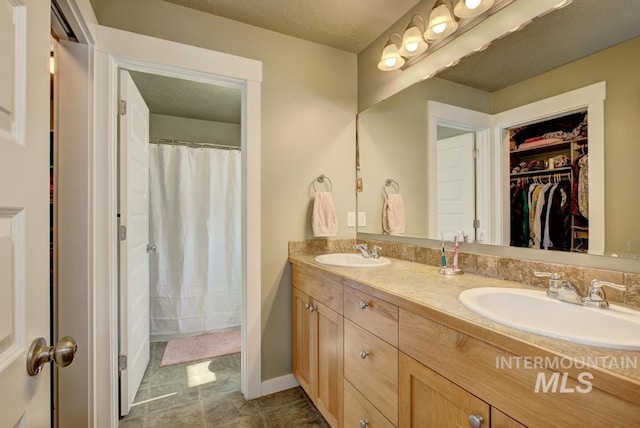 bathroom featuring double vanity, a spacious closet, baseboards, and a sink