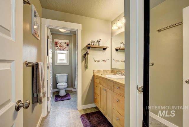 bathroom with toilet, a textured ceiling, vanity, and baseboards