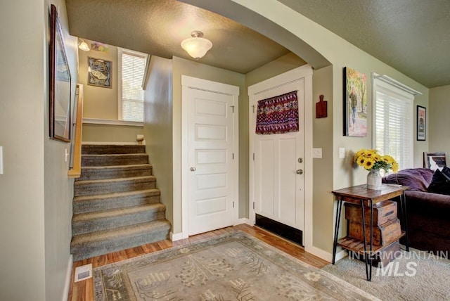 entrance foyer featuring wood finished floors, visible vents, baseboards, arched walkways, and stairs