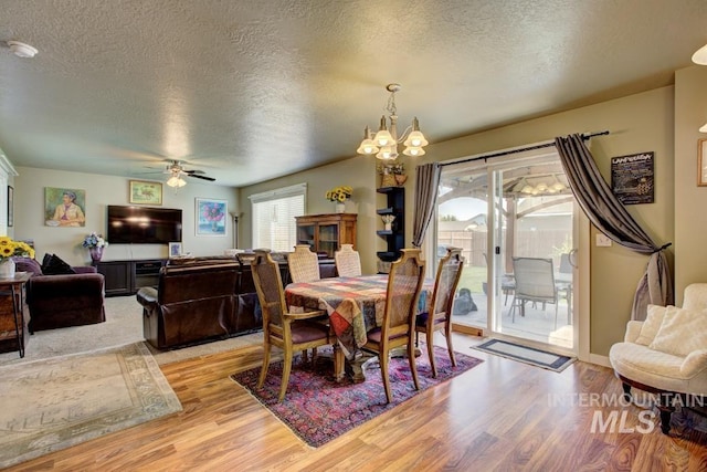 dining space with ceiling fan with notable chandelier, light wood-style floors, and a textured ceiling