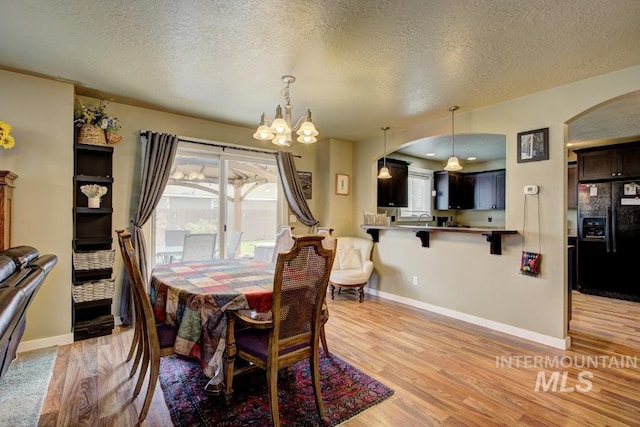 dining space with light wood-style floors, arched walkways, and baseboards