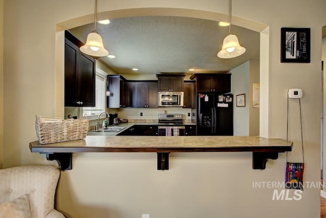 kitchen with a sink, a textured ceiling, stainless steel appliances, dark brown cabinetry, and a breakfast bar area