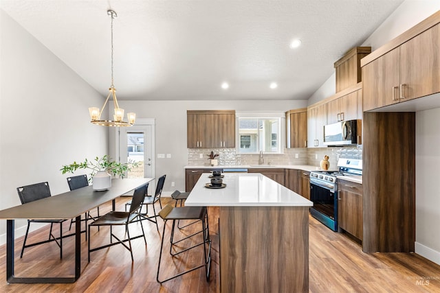 kitchen featuring a kitchen bar, tasteful backsplash, a sink, light wood-style flooring, and appliances with stainless steel finishes