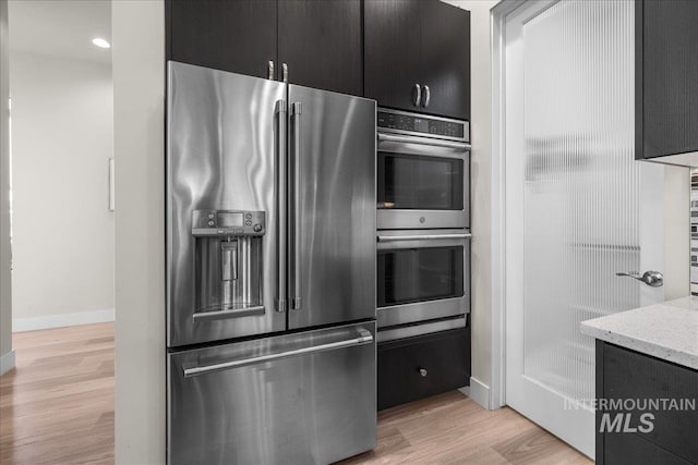 kitchen with appliances with stainless steel finishes, light wood-type flooring, and light stone counters