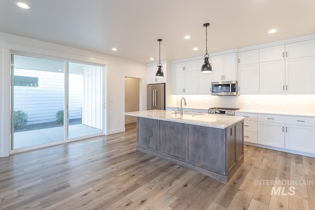 kitchen with appliances with stainless steel finishes, an island with sink, sink, white cabinets, and hanging light fixtures