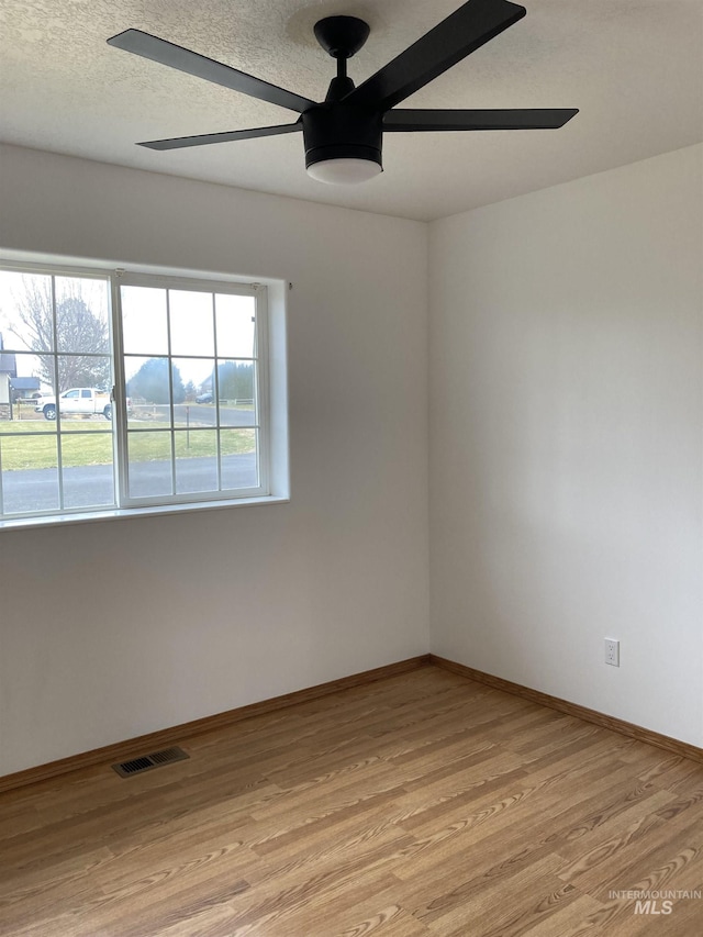 unfurnished room featuring baseboards, visible vents, light wood-style flooring, ceiling fan, and a textured ceiling