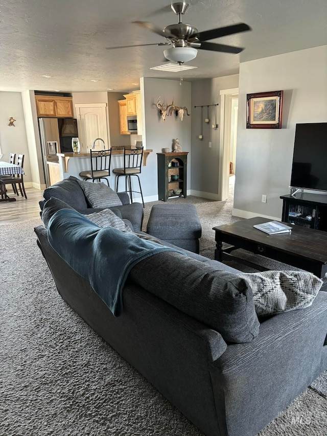 living room with carpet floors, a textured ceiling, and ceiling fan