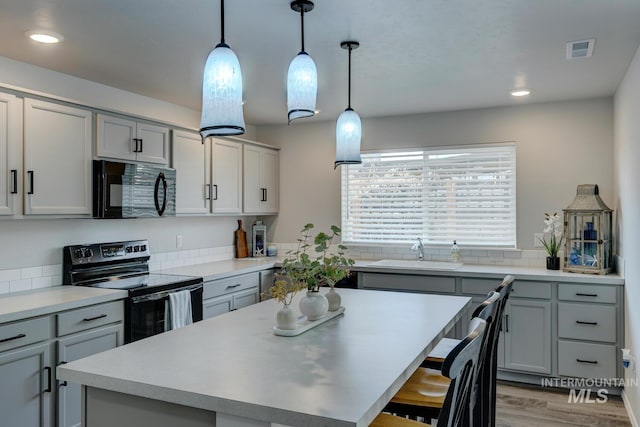 kitchen with a sink, visible vents, black appliances, and gray cabinetry